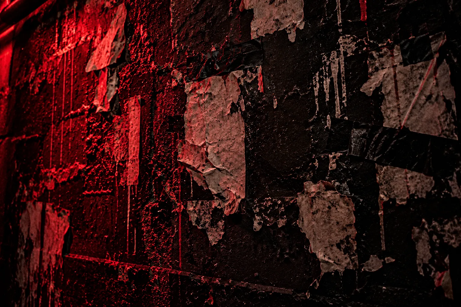 Schwarze Backstage-Wand mit abgerissenen Konzertplakaten und Klebeband im roten Licht